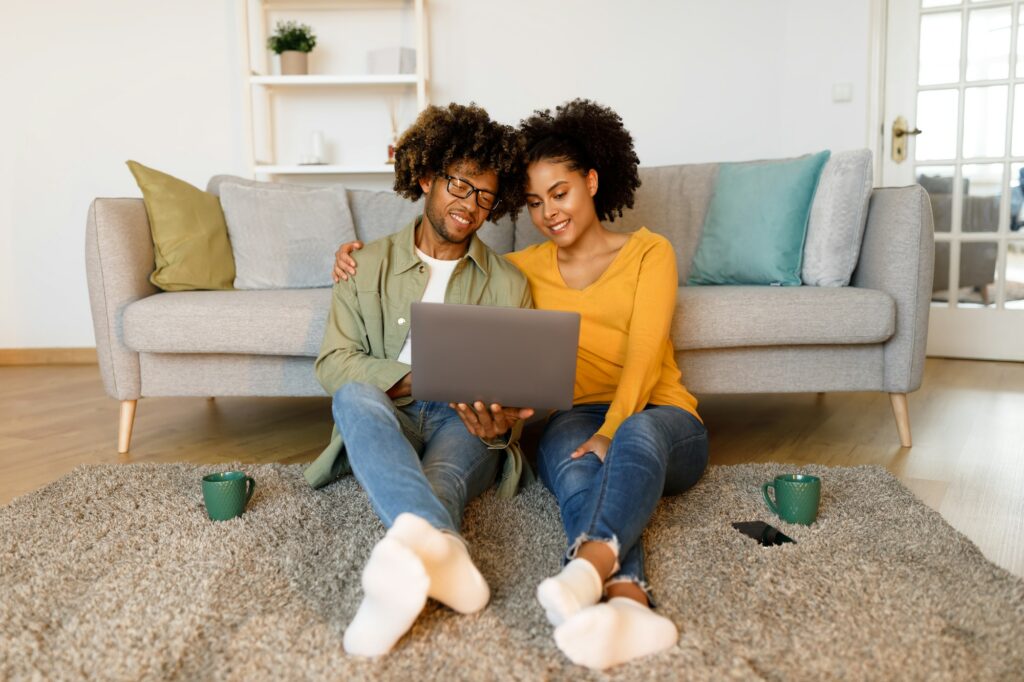African American Couple Using Laptop Sitting On Floor At Home