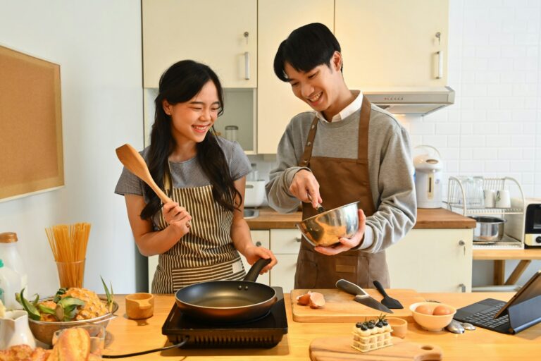 Happy Asian couple preparing dough for pancakes in the kitchen, enjoying leisure time together