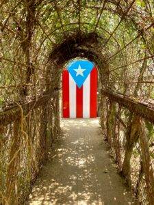 Vertical shot of an arch covered in crawling plants with the flag of Puerto Rico in a park
