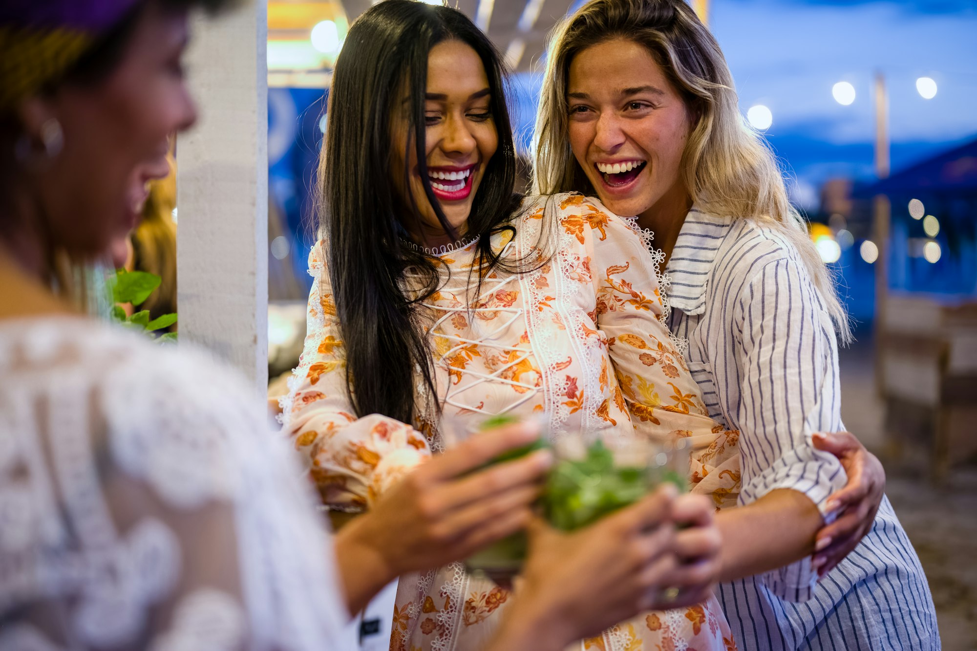 Happy girls having fun cheering with cocktails at bar on the beach, nightlife and luxury lifestyle