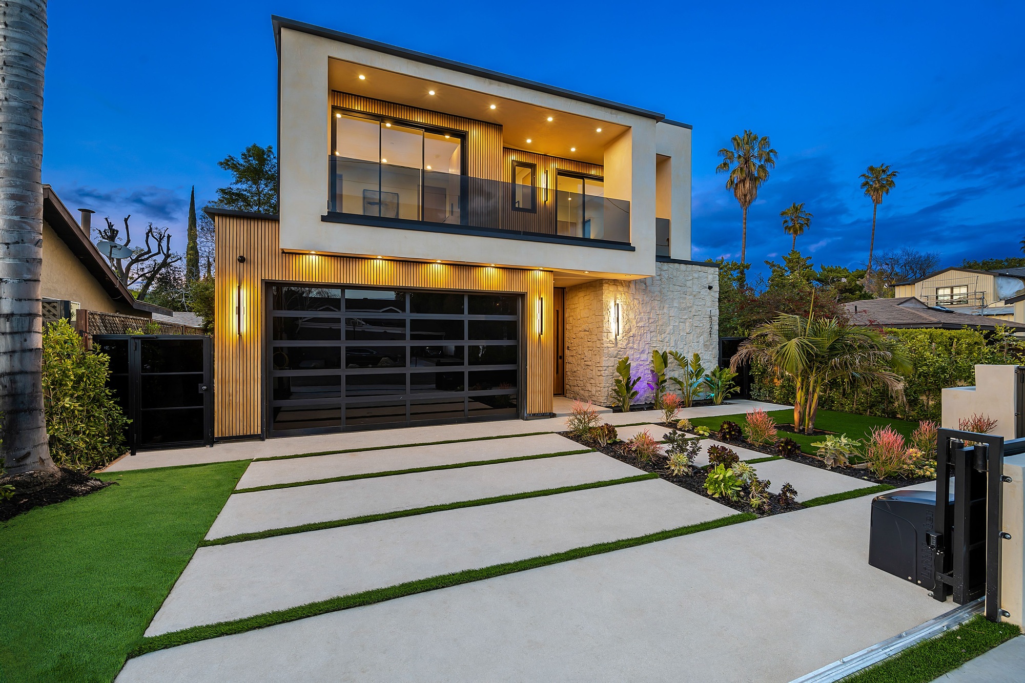 Modern two-story house with large windows and palm trees at dusk.