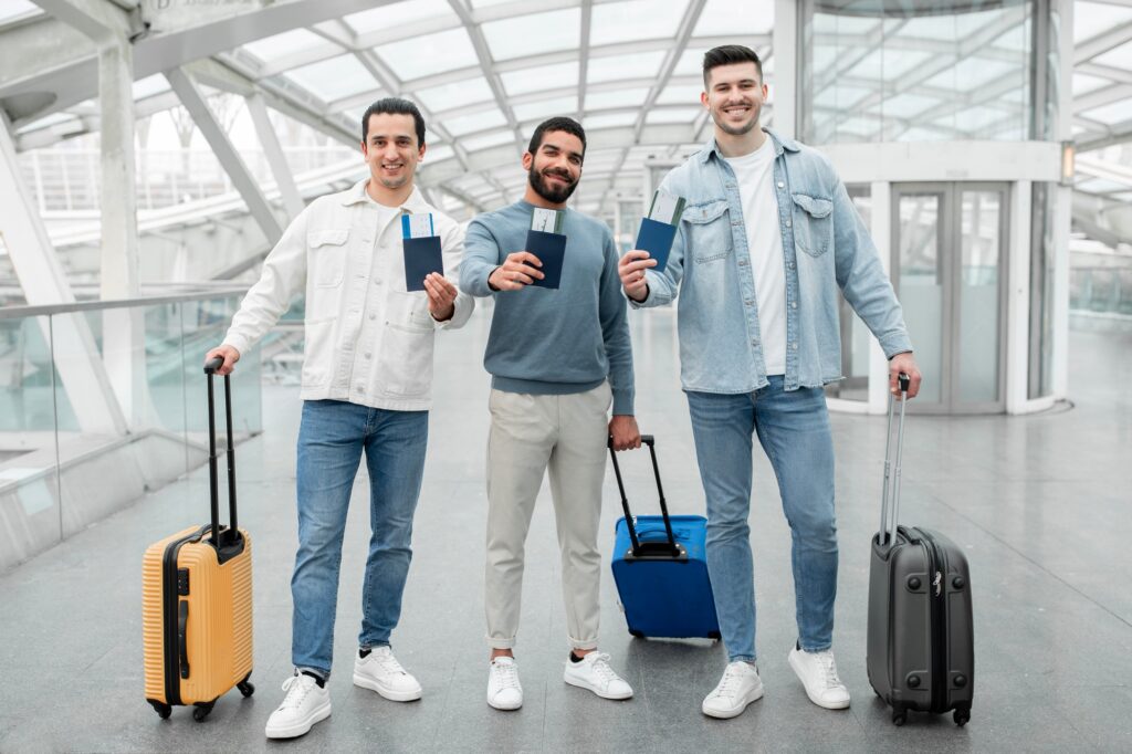 Happy Men Travelers Posing With Luggage Showing Passports In Airport