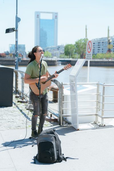 vertical image of young long haired busker man playing guitar and singing in Puerto Madero Argentina vertical image of young long haired busker man playing guitar and singing in Puerto Madero Argentina